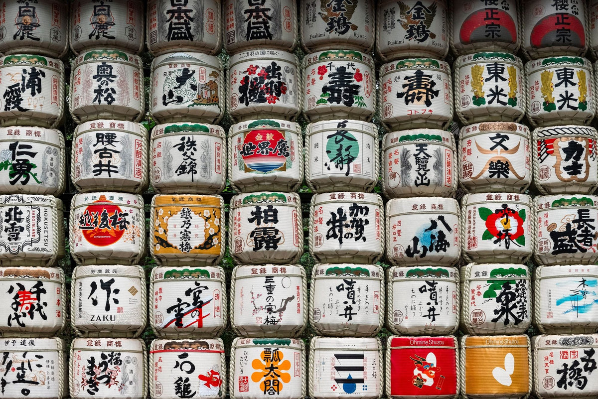 A wall of decorated sake barrels stacked several rows high, each wrapped in straw and painted with a brewery's name in calligraphy.