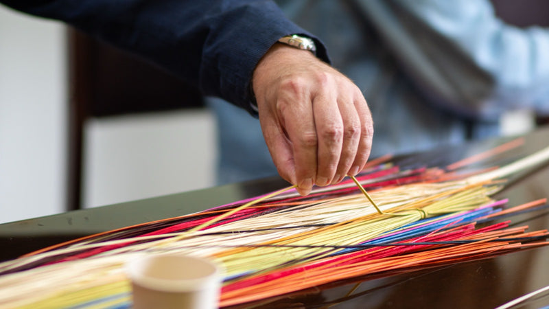 A craftsman's hand drawing a single strand from a bundle of coloured cords
