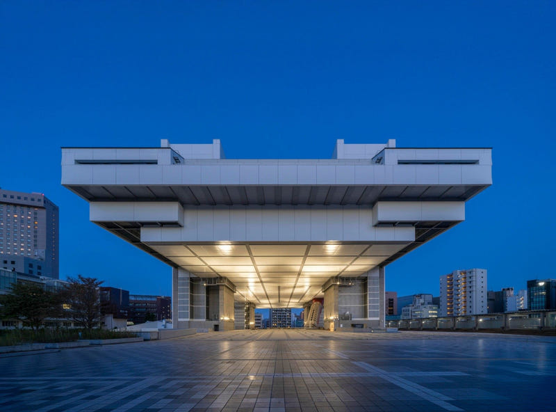 The Edo-Tokyo Museum in Ryogoku at dusk, its white upper block raised high on massive pillars and lit from beneath above an empty plaza.