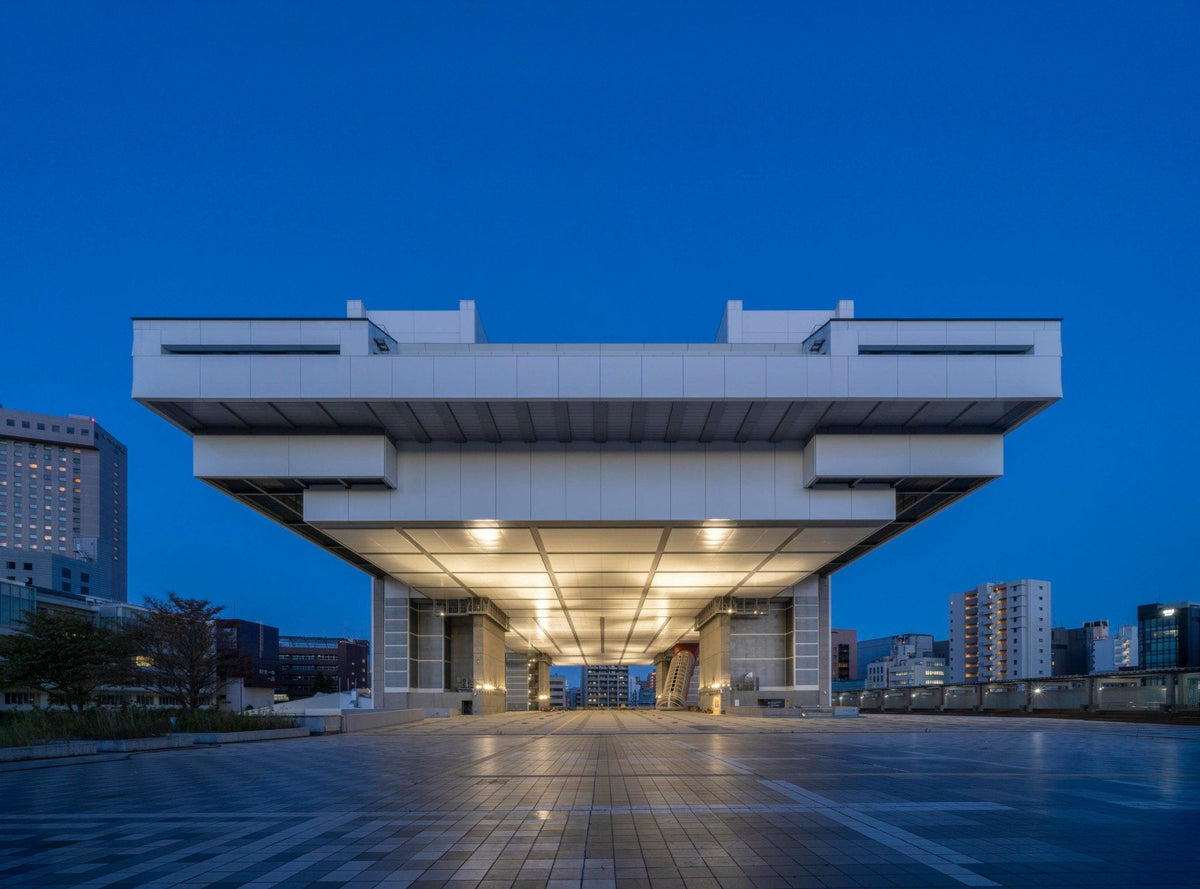 The Edo-Tokyo Museum in Ryogoku at dusk, its white upper block raised high on massive pillars and lit from beneath above an empty plaza.