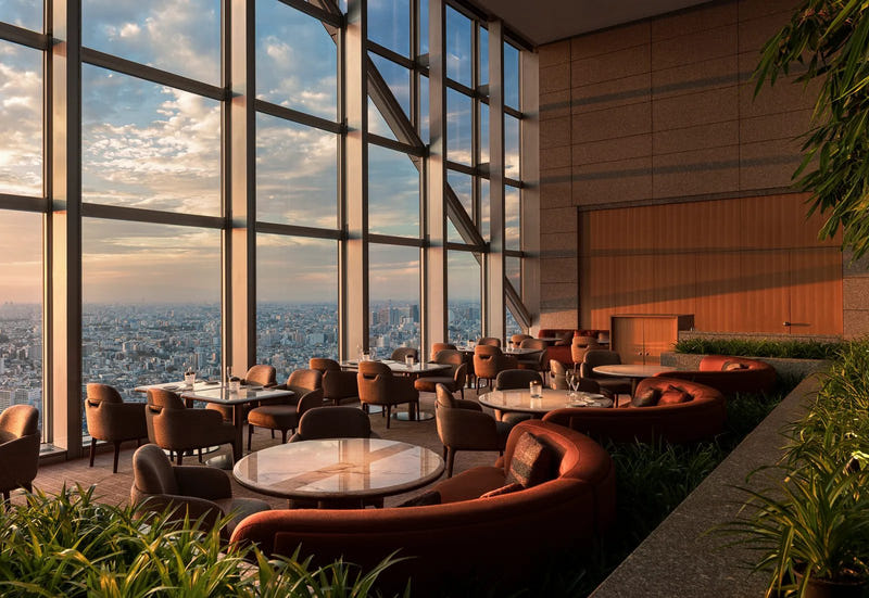 A renovated lounge at Park Hyatt Tokyo at sunset, with curved terracotta banquettes, marble tables and floor-to-ceiling windows over the Tokyo skyline.