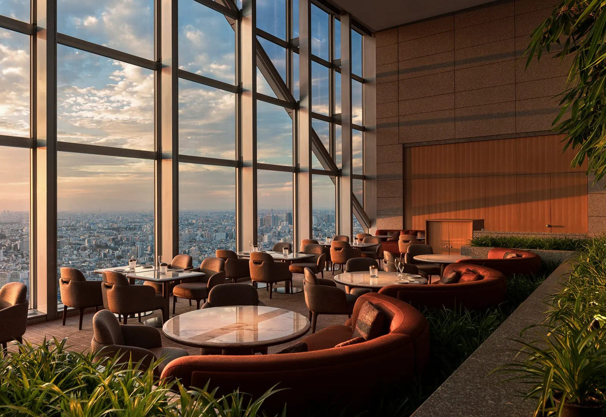A renovated lounge at Park Hyatt Tokyo at sunset, with curved terracotta banquettes, marble tables and floor-to-ceiling windows over the Tokyo skyline.