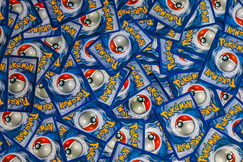 A scattered pile of Pokémon trading cards lying face down, showing the blue card back with the red and white Poké Ball.