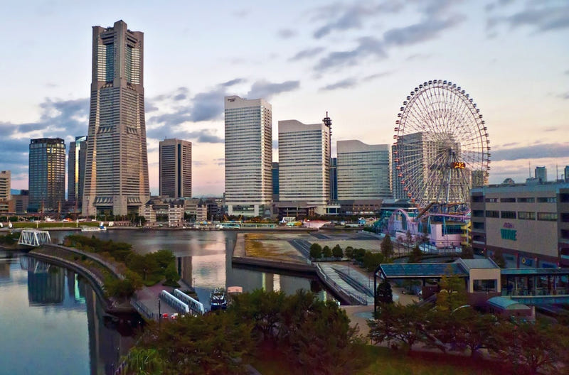 The Minato Mirai skyline at dusk, with Landmark Tower, waterfront hotels and the Cosmo Clock Ferris wheel reflected in the harbor.