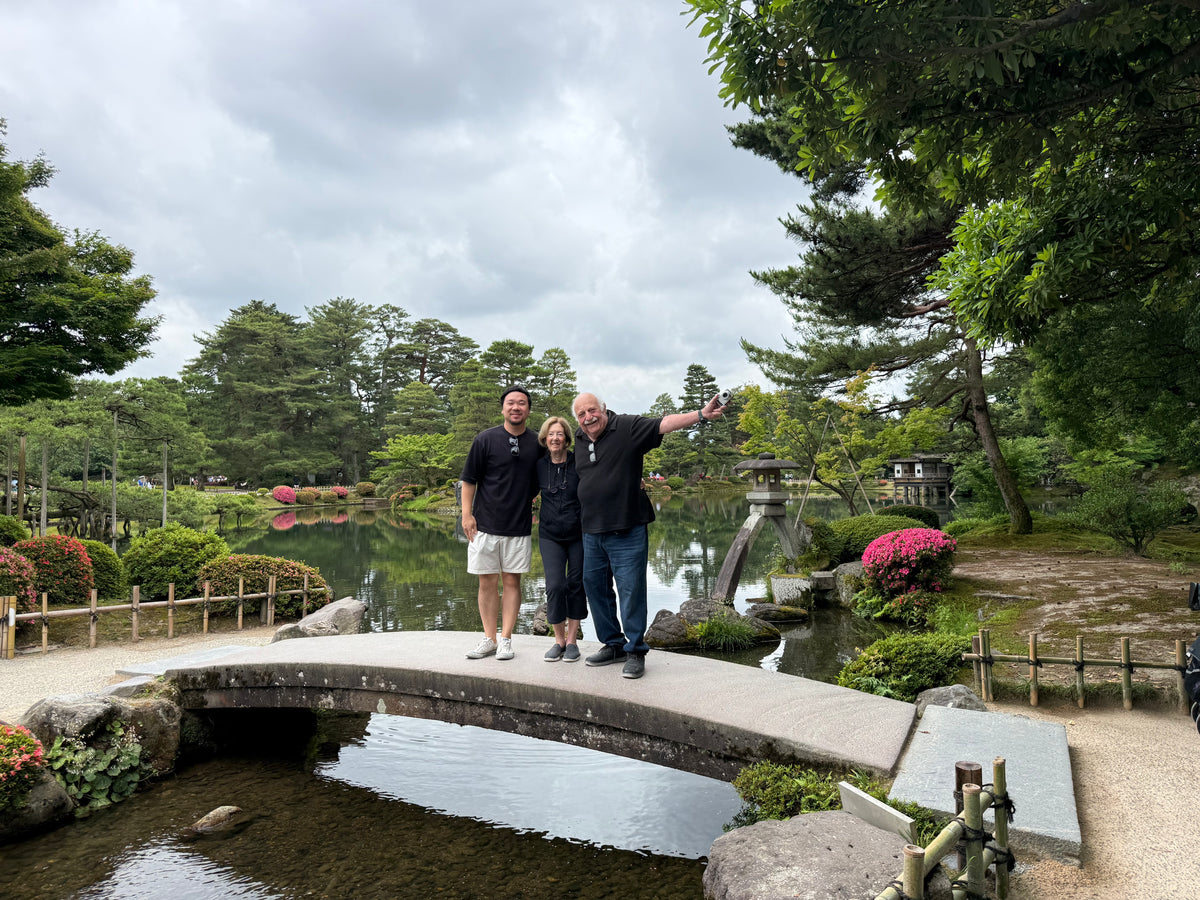 Roy Masuko with two clients on an arched stone bridge in a Japanese garden.