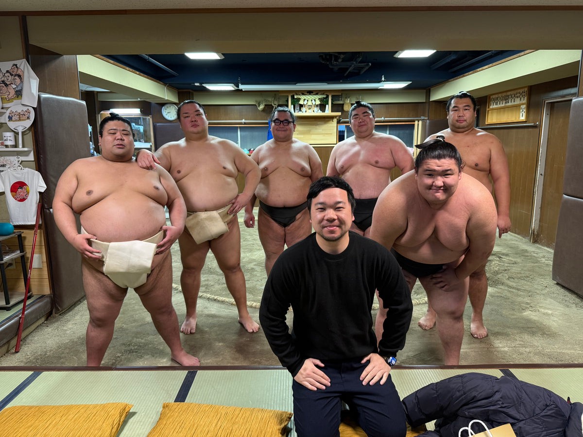 Roy Masuko with six sumo wrestlers in a practice room.