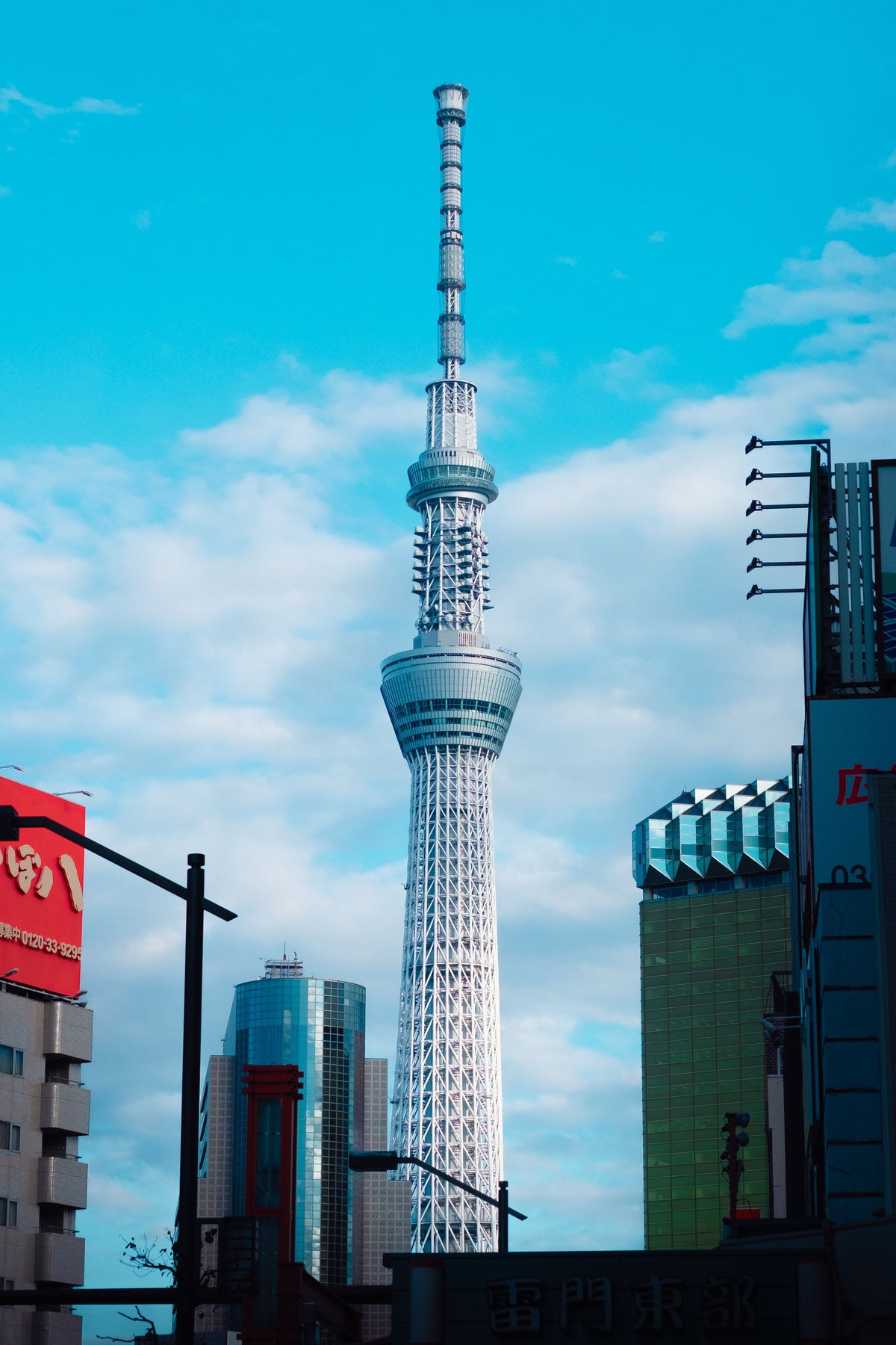 Tokyo Skytree rising above neighboring buildings under a blue sky.