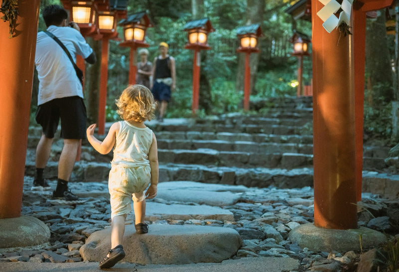 Young child walking through a lantern-lined shrine approach in Japan.