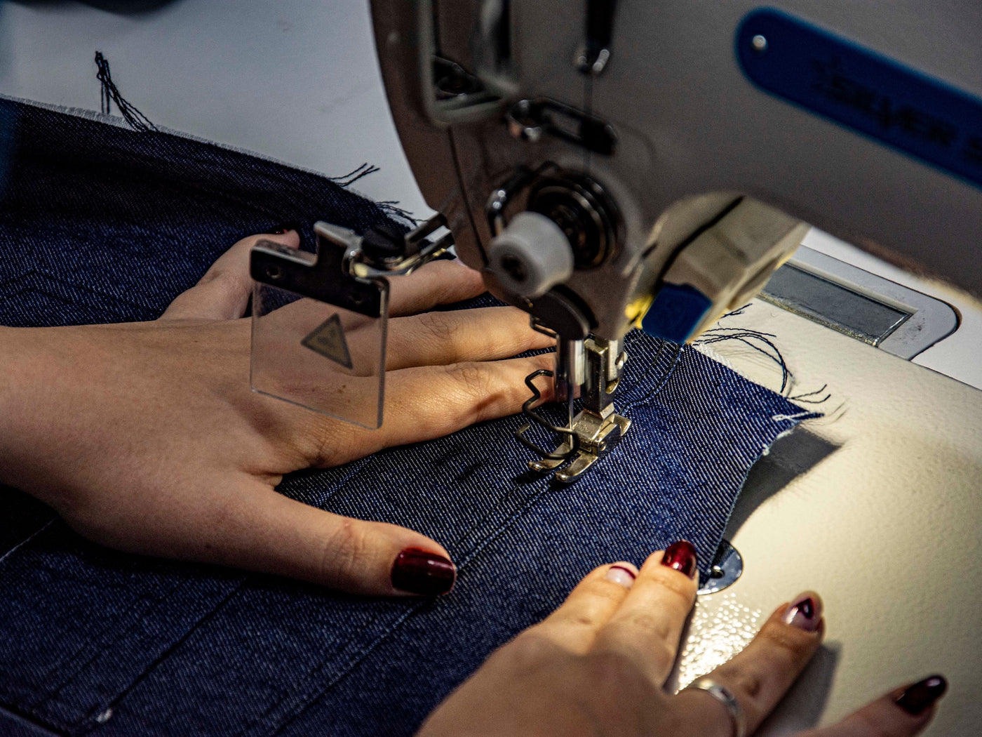 Hands guiding indigo denim through a sewing machine